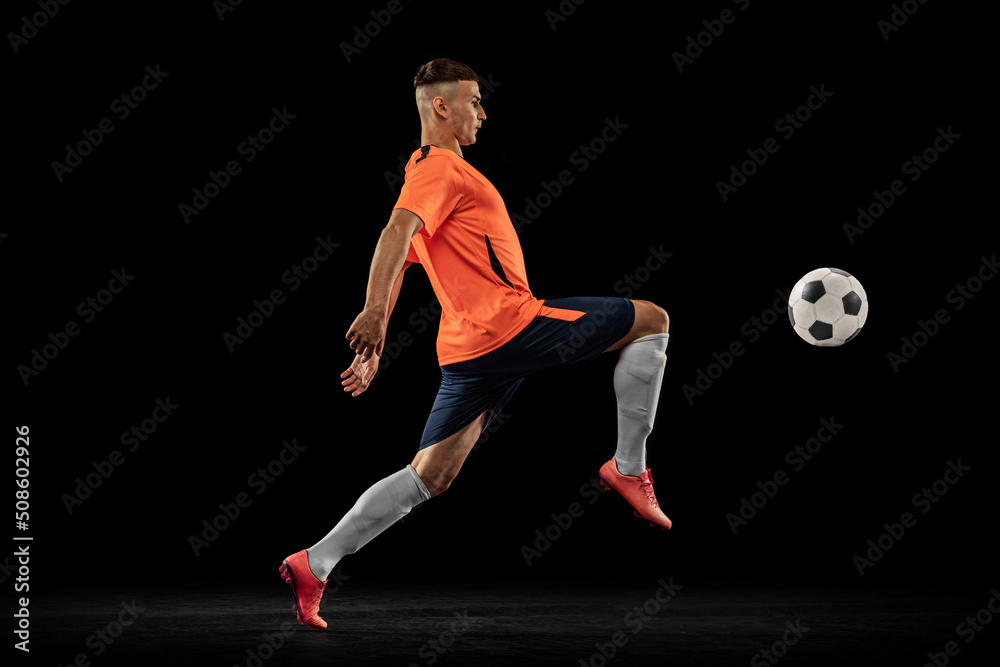 Dynamic portrait of professional male football soccer player in motion isolated on dark background. Concept of sport, goals, competition, hobby, achievements Dynamic portrait of professional male football soccer player in motion isolated on dark background. Concept of sport, goals, competition, hobby, achievements