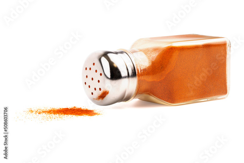 glass pepper pot with powdered red pepper inside dropped on its side isolated on white background, some pepper spilled photo