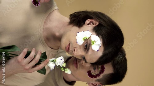 young gay couple with white eustoma flower and petals on faces isolated on beige photo