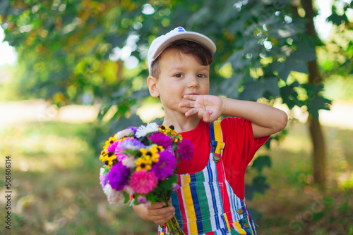 a boy in bright clothes with flowers in his hands against the background of nature. park. 