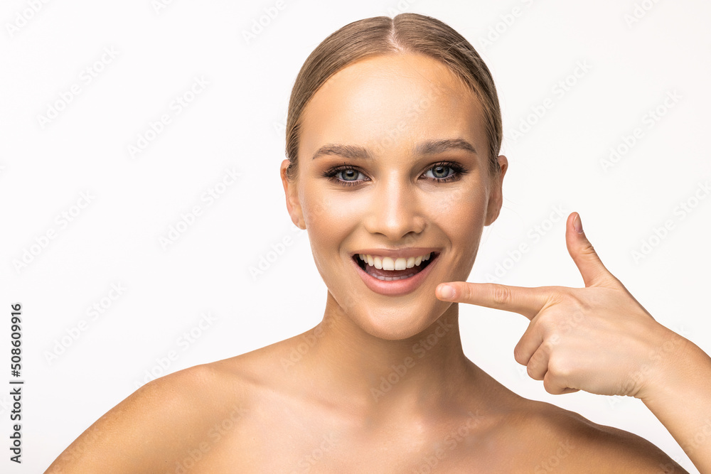 Young woman with perfect skin, bright spring pink make-up and naked shoulders on a white background. Pointing fingers at snow-white teeth. Young woman with perfect skin, bright spring pink make-up and naked shoulders on a white background. Pointing fingers at snow-white teeth.