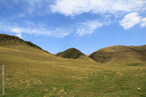 Mountains with gentle slopes with grass on the Assy plateau in autumn against a sky with clouds