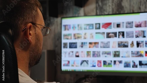 Close-up of a bearded man wearing glasses at night watching erotic photos on the monitor screen. Sexual addiction. Sex alone. Male masturbation
