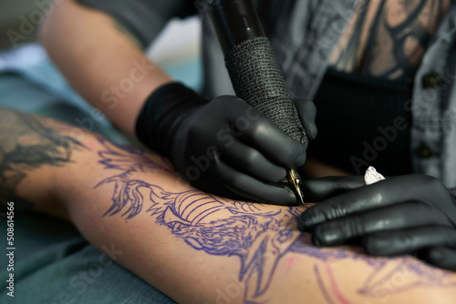 Close up of tattoo artist drawing on arm of client photo