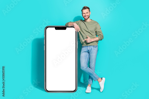 Photo of confident man direct finger white card empty space wear pullover jeans isolated blue color background © deagreez
