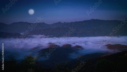 4K timelapse. Scenic landscape of stars, meteors and full moon moving over mountains at night. Sky in wild misty nature with wave of low clouds blowing over decorate the beautiful scenery. 4096x2304