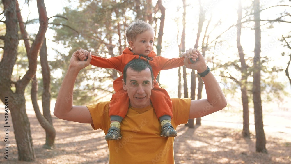 Obraz premium father and son in the park. happy family piggyback a kid dream concept. father holds baby son keeps on the neck in a forest park close-up. baby and parent man happy family fun walking in nature