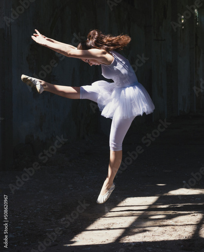 Young ballerina in white tutu dancing and jumping in abandoned building on a sunny summer day