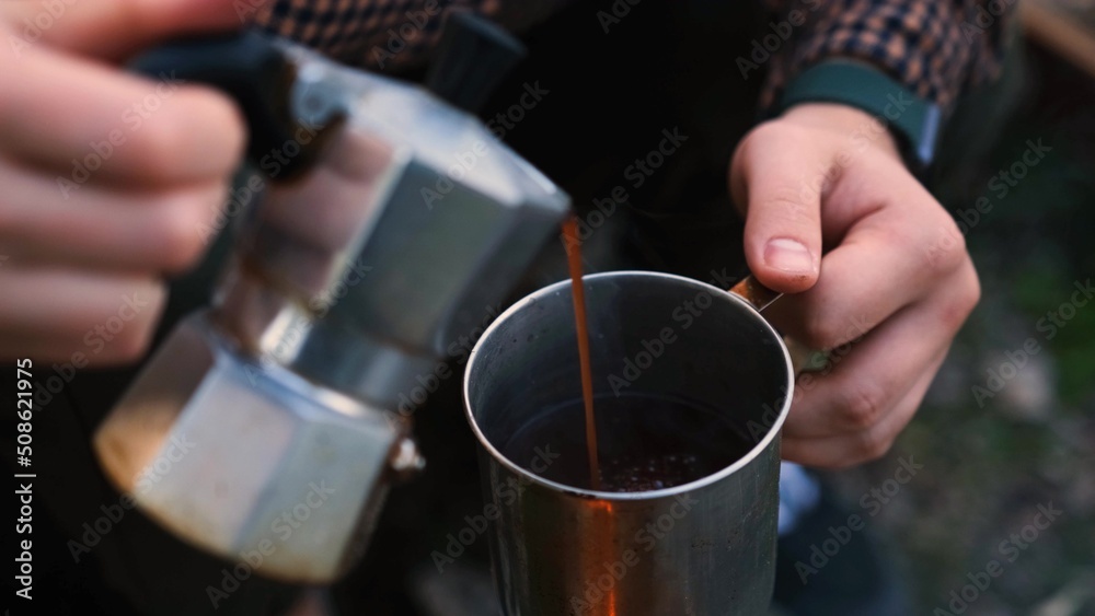 Young pair in forest. Woman pours tea, coffee from a Aluminium Coffee Maker. Camping couple pouring coffee in a cup.