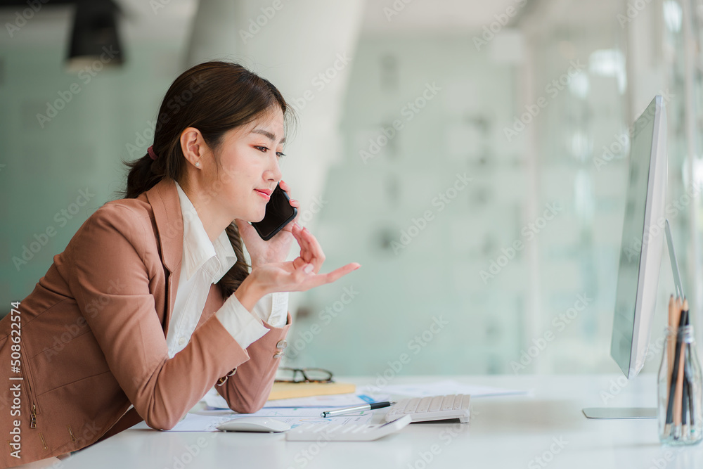 Young Asian businesswomen holding a phone can work with a computer with the company's financial graph analysis, and accounting calculations. Young Asian businesswomen holding a phone can work with a computer with the company's financial graph analysis, and accounting calculations.