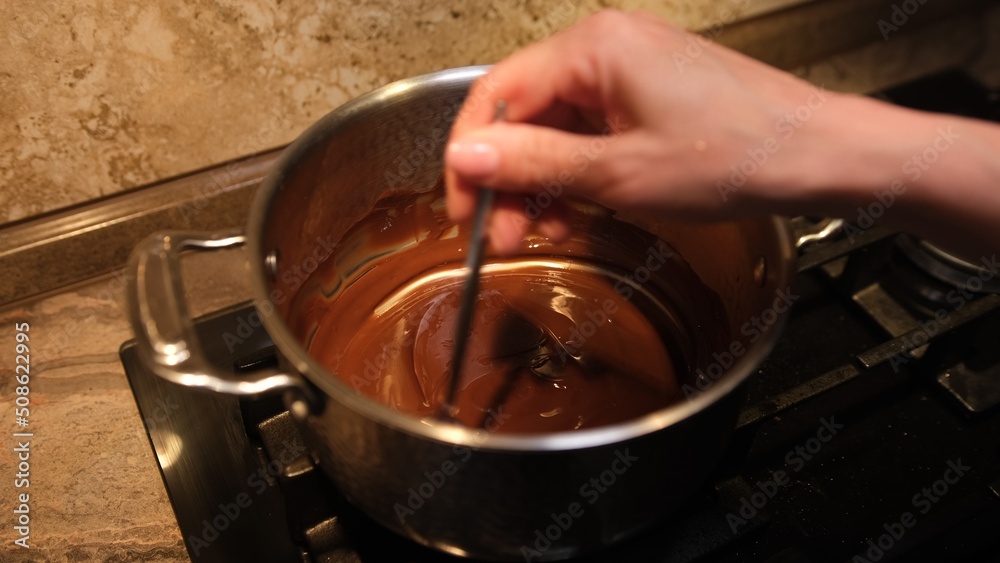Woman mixing smooth delicious dark chocolate ganache with whisk in silver bow