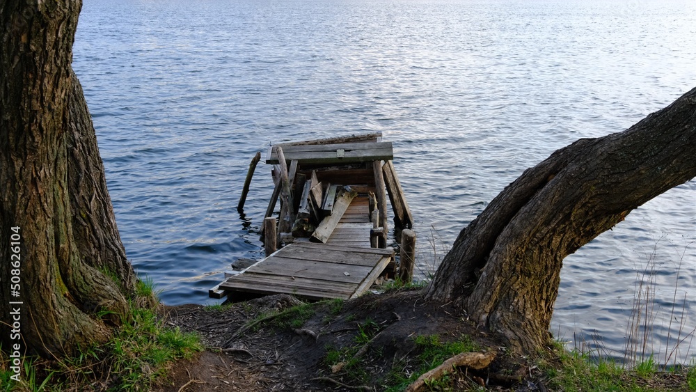 Fototapeta premium Autumn scene - lake and destroyed wooden pier. Old rotten wooden pier with missing planks with bench on a lake in the forest at autumn.