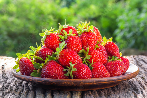 Fresh ripe strawberries in a plate on a wooden table in the garden