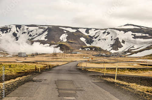 Hengill, Iceland, April 22, 2022: landscape near the Hellisheiði geothermal power plant, with mountains, an asphalt road, steam and power lines photo