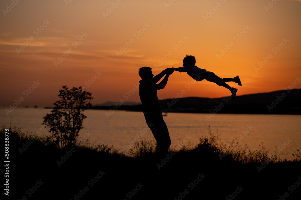 Father and son playing on the seashore at the sunset time in summer and enjoying the sunset. Summer adventure, fun trip with kids. Fatherhood, Father's Day. Happy family travel and vacation concept
