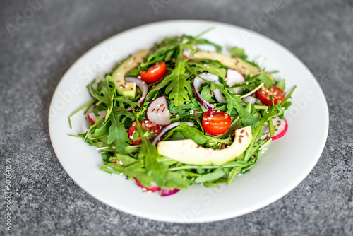 Vegan food. Healthy fresh vegetable salad - tomatoes, arugula, avocado, radish on a stone background. Diet menu.