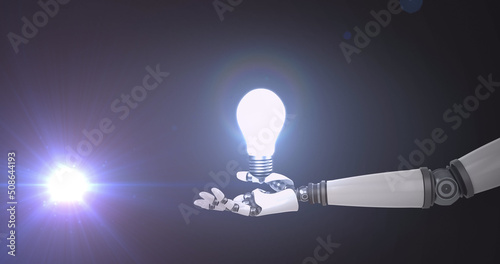 Image of illuminated light bulb over hand of extended robot arm and light on dark background