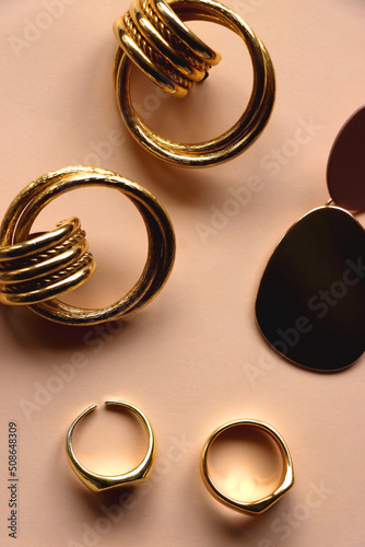 Various gold jewelry and pearl hair clips on peach colored background. Flat lay.