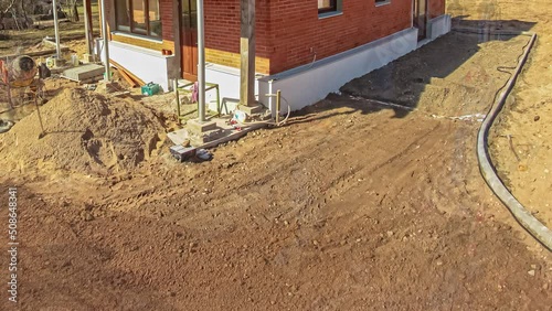 Shot over landscape transform in front of a house in timelapse. View of a wooden house on a construction site with bulldozer levelling the land beside the house.