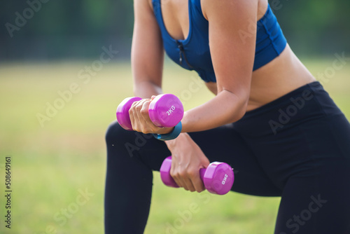 Asian woman in sport clothes with smart watch on hands workout with dumbbell at park