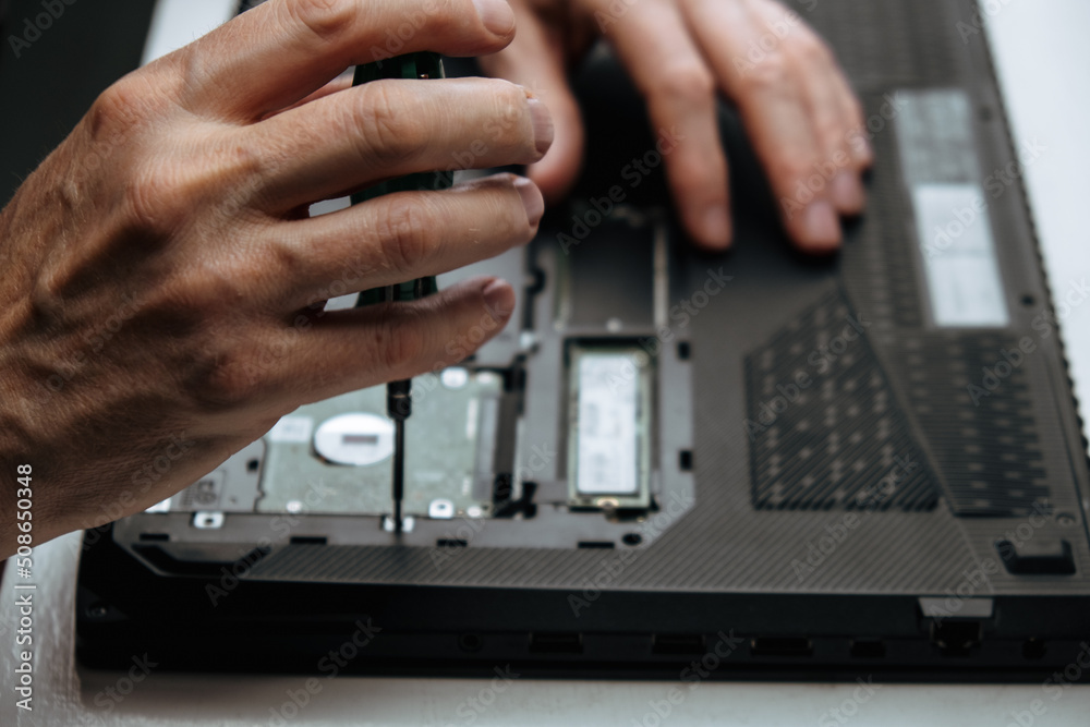 close-up of repairman's hands installing hard drive into laptop case with screwdriver after repair and maintenance. fixing the disk with screws using screwdriver. laptop maintenance. selective focus.