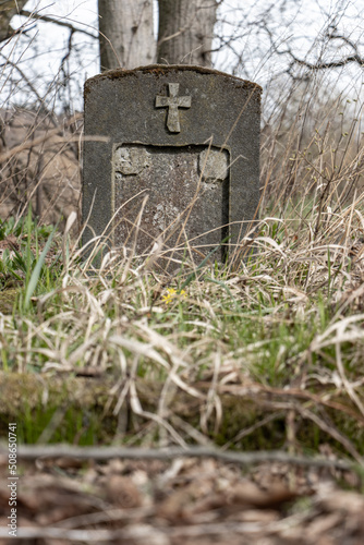 A derelict stone tombstone with a cross in an abandoned cemetery