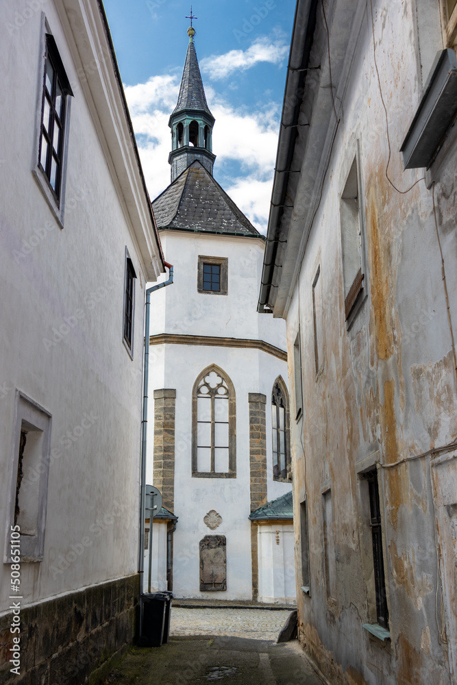 A narrow street between old houses with view at the church, Czechia.