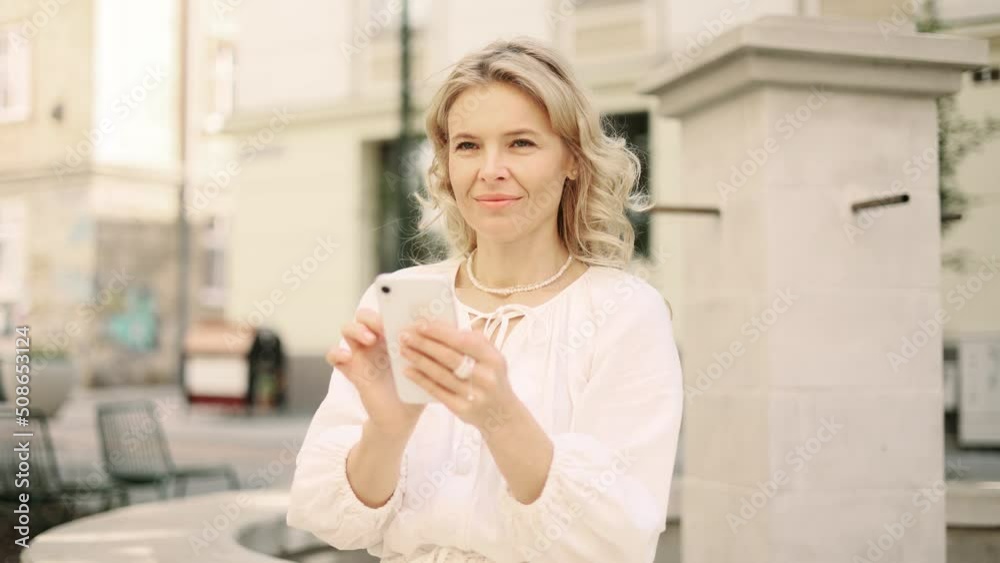 Close up attractive caucasian middle agedwoman hold smartphone, watching social media standing on a city street. Smiling woman texting on her phone. Close up attractive caucasian middle agedwoman hold smartphone, watching social media standing on a city street. Smiling woman texting on her phone.