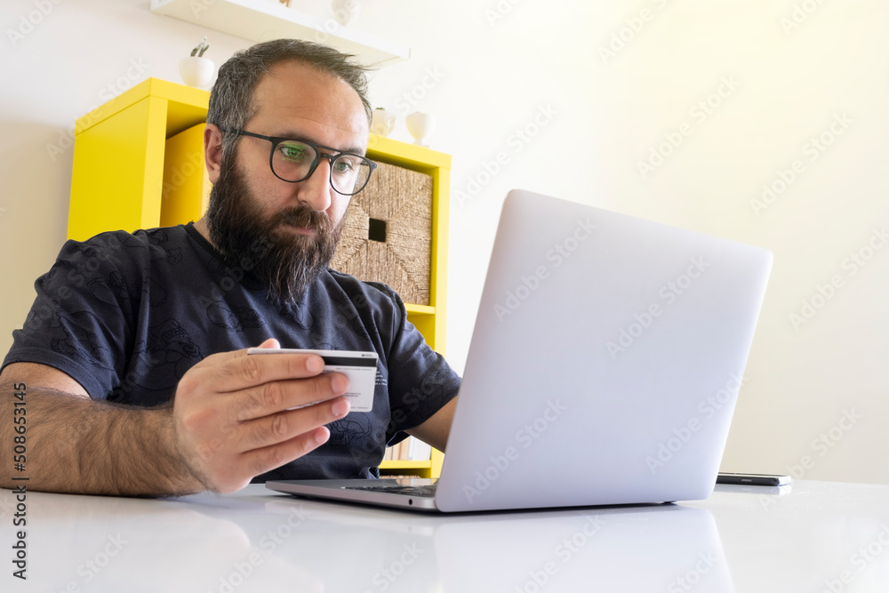 Doing online shopping, young serious bearded young male doing online shopping. Providing online payment at the office or working from home. E-commerce concept idea photo with copy space. Doing online shopping, young serious bearded young male doing online shopping. Providing online payment at the office or working from home. E-commerce concept idea photo with copy space.