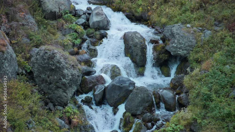 Beautiful waterfall flowing above the big boulders with autumn colors vegetation surrounding it. Slow motion. Beautiful waterfall flowing above the big boulders with autumn colors vegetation surrounding it. Slow motion.