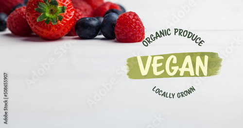 Image of vegan text in green over fresh organic berries on white background