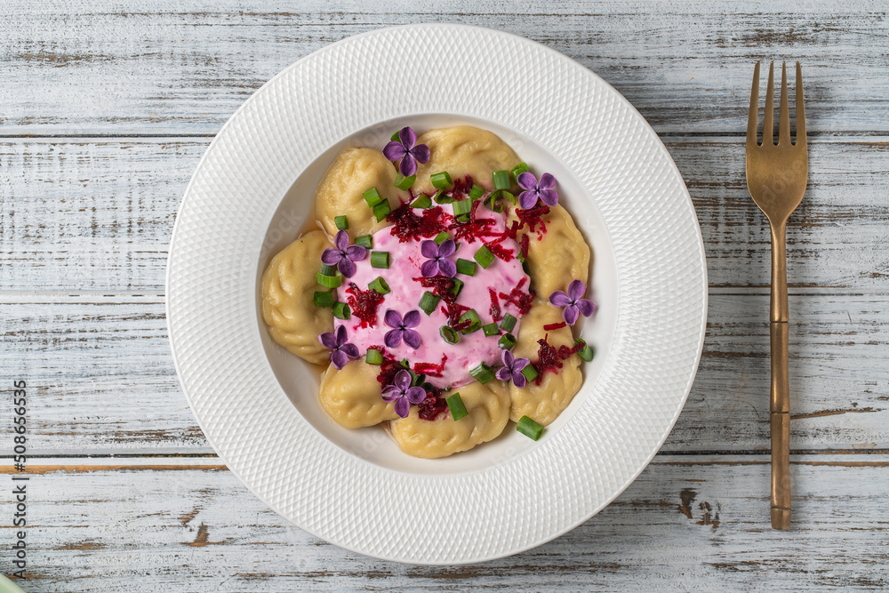 Appetizing dumplings stuffed with potatoes and mushrooms with sour cream decorated with beets and lilac flowers Appetizing dumplings stuffed with potatoes and mushrooms with sour cream decorated with beets and lilac flowers