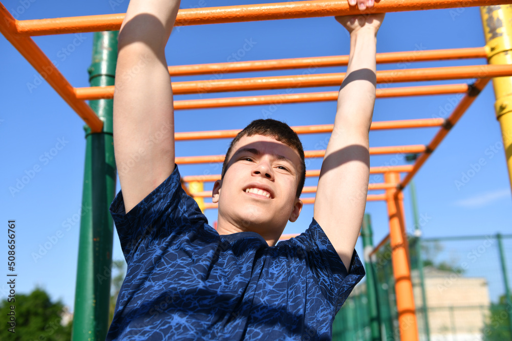 Fototapeta premium a teenage boy trains on a sports ground outdoors, he does physical exercises, a healthy lifestyle, a bright sunny day in summer