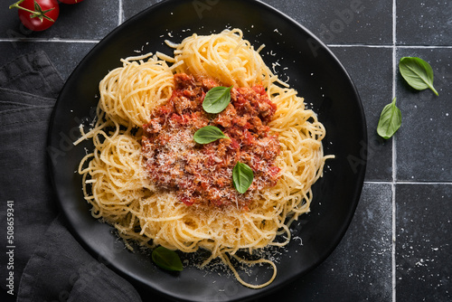 Tagliatelle pasta with meatballs in tomato sauce, basil and parmesan cheese on black stone or concrete background. Traditional Italian dish and cuisine. Top view with copy space.