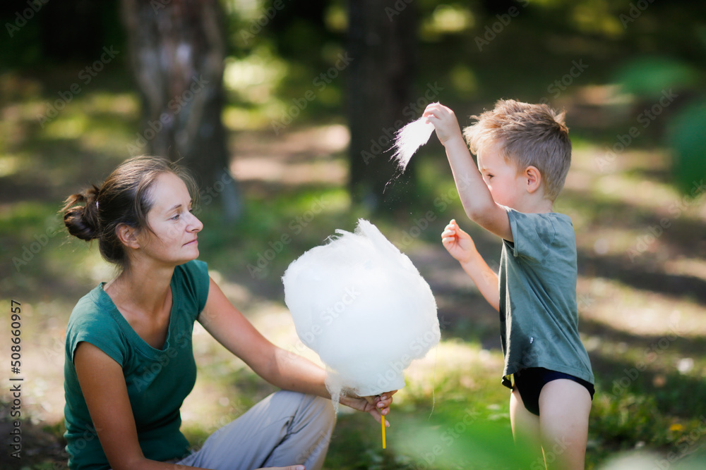 Obraz premium Cute european boy son and mom eating cotton candy in the park together, lifestyle