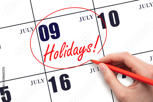 Hand drawing a red circle and writing the text Holidays on the calendar date 9July. Important date. photo