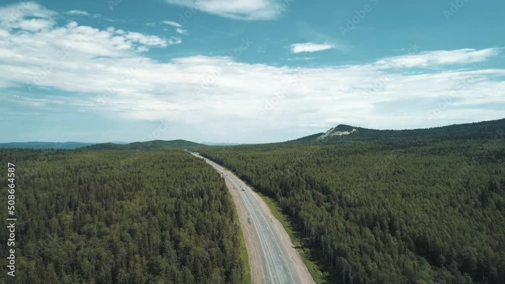 Aerial view of an intercity highway with traffic going through a green pine forest on bright sunny day. High altitude panoramic shot Aerial view of an intercity highway with traffic going through a green pine forest on bright sunny day. High altitude panoramic shot