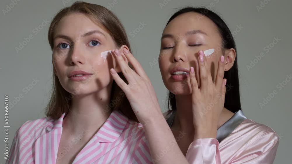 Two young ladies applying cream on cheeks. Closeup of ideal beautiful woman faces. Young women portrait with cream on ckin. Skin care procedure Two young ladies applying cream on cheeks. Closeup of ideal beautiful woman faces. Young women portrait with cream on ckin. Skin care procedure