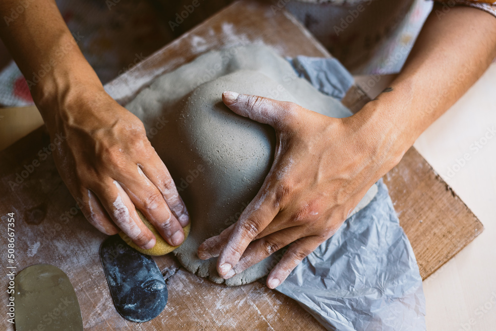Close up of woman hands working clay making pottery at home. Concept of hobby and creativity at home. Kneading and moistening the clay.