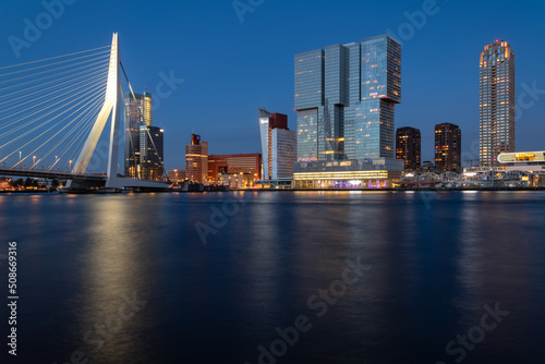 Rotterdam nighttime panorama with “Erasmus-Bridge“ over river Nieuwe Maas at evening blue hour in South Holland Netherlands. Waterfront with illuminated bridge and tall buildings on the waterfront.