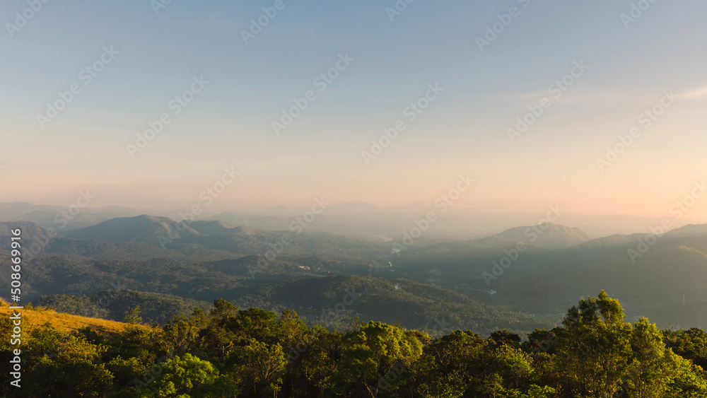 Cardamom hills under clear sky with mist on horizon at sunset in Thekkady, India.