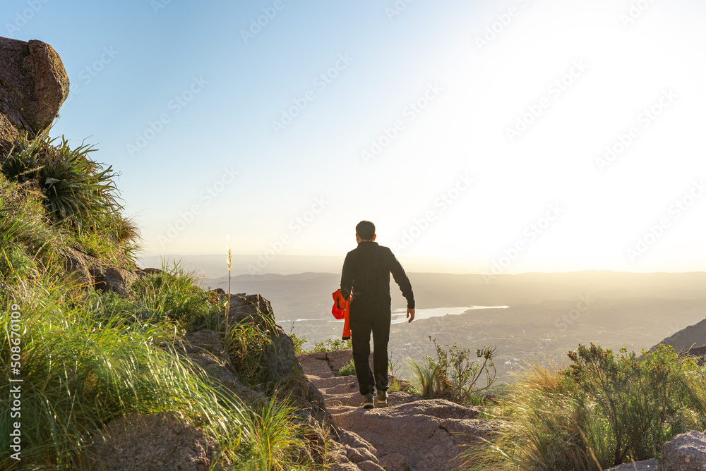 Rear View of Young Tourist Man Walking on a Path in the Edge of a Mountain at Sunset Time