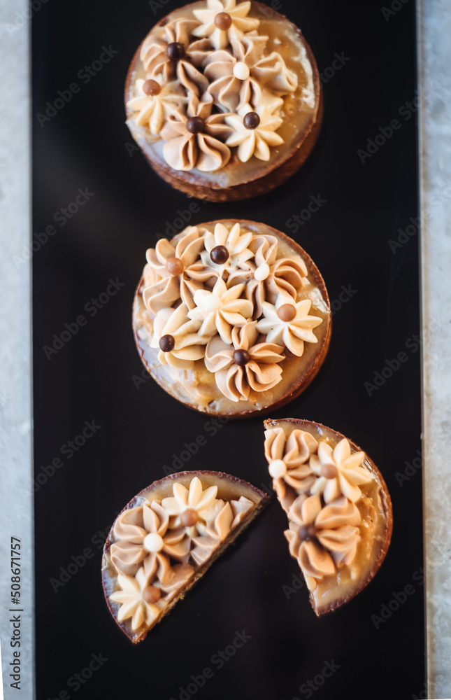 Shortbread tartlets with salted caramel, nuts and cream. Sweet chocolate cakes isolated on black background. Modern mini desserts for candy bars, parties. View from above