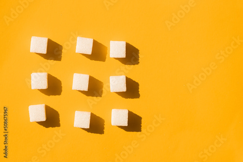 Pointer of white sugar cubes on yellow background