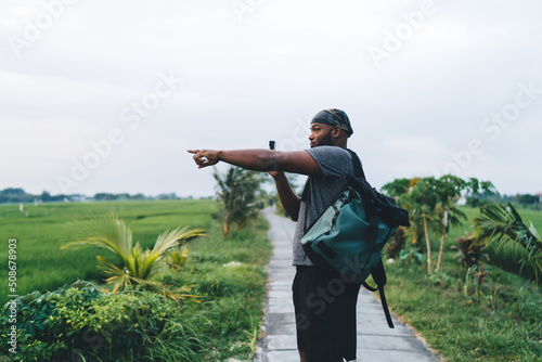 African American travel blogger with touristic backpack using go pro technology for shooting vlog content and talk about summer vacations at Bali, hipster guy pointing at rice fields in Indonesia #508678903