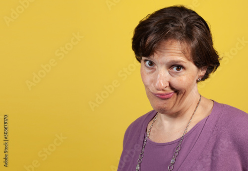 Incredulous attractive mature woman in purple blouse on a yellow background looking at the camera photo