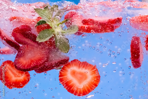Sliced Strawberry in water with water splash and air bubbles on blue background. Close up image.