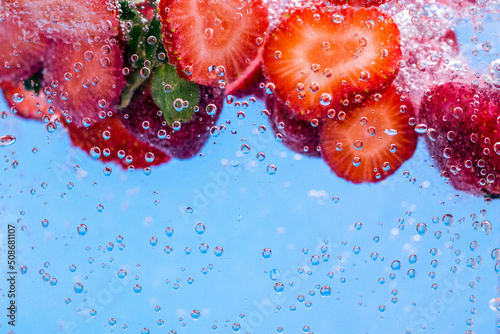 Sliced Strawberry in water with water splash and air bubbles on blue background. Close up image.