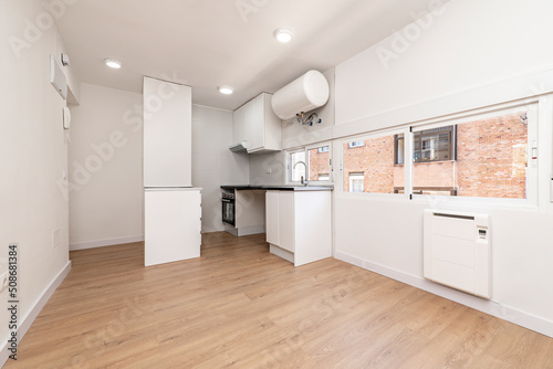 Kitchen with white cabinets and a glossy black countertop with a hardwood floor and windows along one wall  a water heater hanging from the ceiling