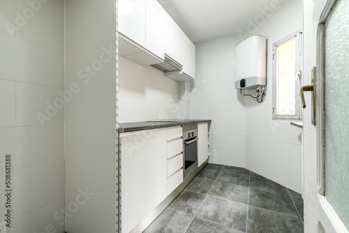 Kitchen with newly installed cabinets and drawers in a simple apartment with gray tile floors, natural gas water heater